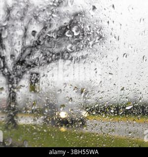 Sfocate silhouette auto visto attraverso gocce di acqua sul parabrezza per auto Foto Stock
