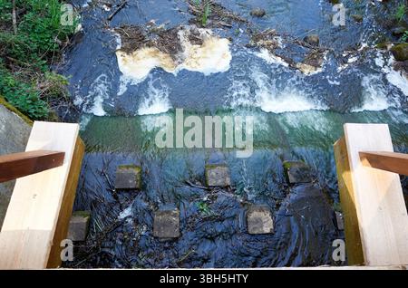 Fiume con un ponte di legno sopra di esso. L'acqua è torbida e il ponte è di legno. Il ponte è vecchio e ha un'atmosfera rustica Foto Stock