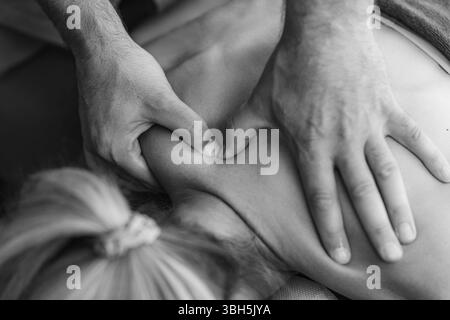 Il fisioterapista esegue un massaggio tissutale profondo sulla spalla del paziente per alleviare la tensione muscolare e migliorare la mobilità in un ambiente terapeutico. Foto Stock