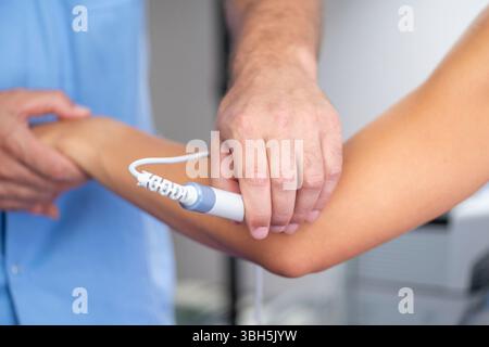 Il fisioterapista utilizza la terapia laser sul gomito del paziente per alleviare il dolore e accelerare la guarigione. Il trattamento laser mira ai tessuti molli per ridurre l'infiammazione e favorire il recupero. Foto Stock