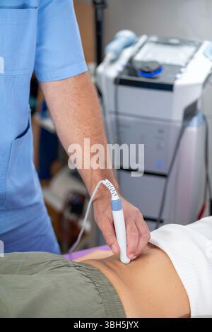 Il fisioterapista utilizza la terapia laser su un paziente nella parte inferiore della schiena per alleviare il dolore, ridurre l'infiammazione e promuovere la guarigione dei tessuti, migliorando la mobilità e il recupero. Foto Stock