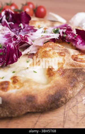 Pizza italiana con insalata di cicoria servita su tagliere rustico in legno. Crosta napoletana. Messa a fuoco selettiva. Primo piano Foto Stock