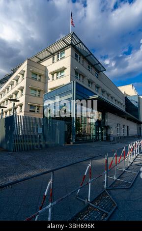Vista verticale dell'ambasciata degli Stati Uniti a Berlino, in Germania, con barriere di sicurezza visibili e la bandiera americana in alto. Foto Stock