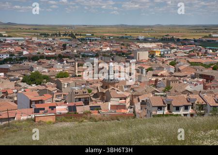 Una vista grandangolare della città di Consuegra, Toledo, mostra tetti di tegole rosse, un'importante chiesa storica e terreni agricoli circostanti sotto un blu brillante Foto Stock