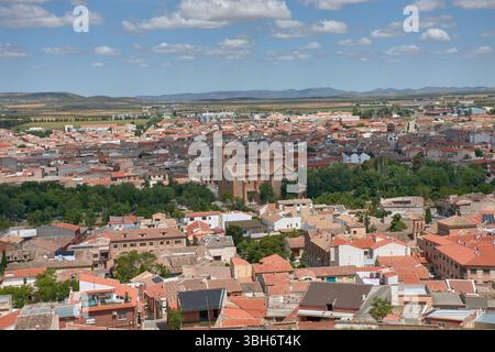 Una vista grandangolare della città di Consuegra, Toledo, mostra tetti di tegole rosse, un'importante chiesa storica e terreni agricoli circostanti sotto un blu brillante Foto Stock