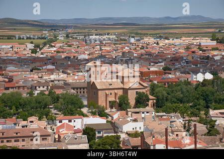Una vista grandangolare della città di Consuegra, Toledo, mostra tetti di tegole rosse, un'importante chiesa storica e terreni agricoli circostanti sotto un blu brillante Foto Stock