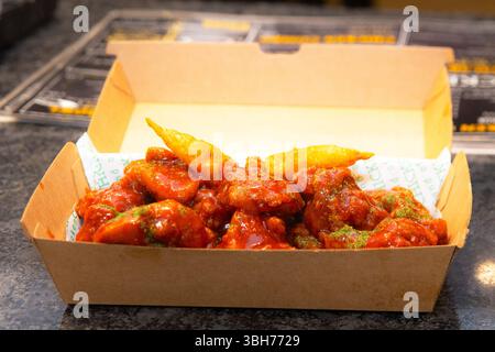 Salsa coreana di pollo rosso piccante essiccato in profondità in una scatola di carta da asporto. Foto Stock