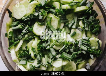 Insalata fresca di cetrioli con cipolla primaverile. Verdure verdi tagliate a fette nel recipiente. Cibo estivo leggero e salutare. Vista ravvicinata degli ingredienti crudi. Foto Stock