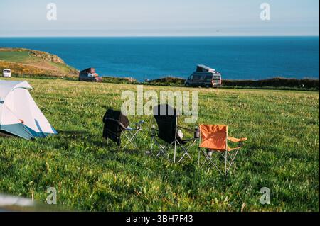 Un gruppo di sedie è allestito in un campo erboso vicino a un corpo d'acqua. Le sedie sono disposte in fila, con una sedia a sinistra, una nel mezzo Foto Stock