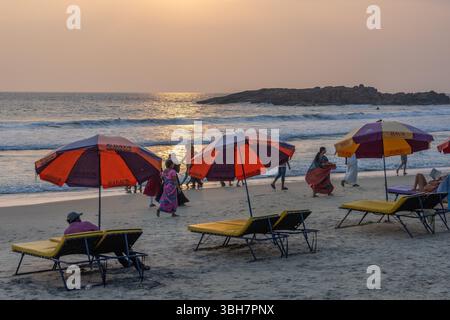 Persone che camminano e si rilassano al tramonto sotto gli ombrelloni a Kovalam Beach, Kerala, India meridionale Foto Stock
