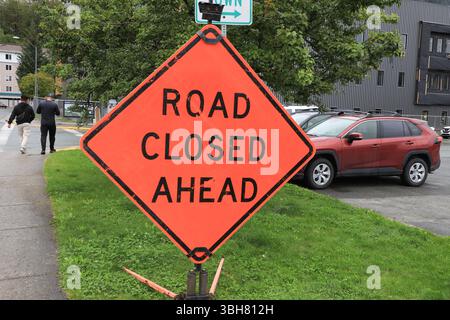 Un cartello arancione Road chiuso davanti a una strada, sul lato di una strada, in una giornata estiva di sole, Foto Stock