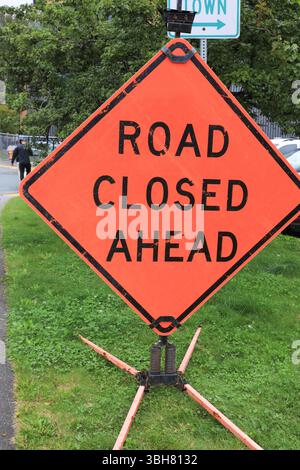 Un cartello arancione Road chiuso davanti a una strada, sul lato di una strada, in una giornata estiva di sole, Foto Stock