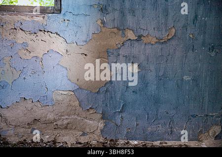Sbucciatura della vernice blu sulla parete di argilla incrinata. Struttura grunge di edifici abbandonati, perfetta per design, background e concetto di decadimento. Foto Stock