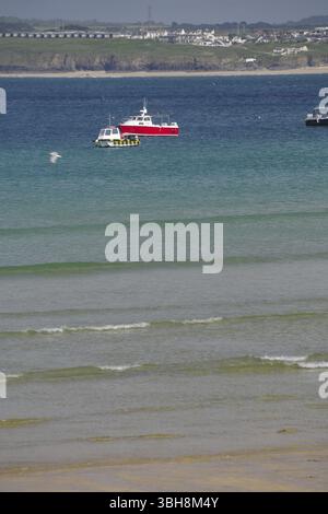 Una barca rossa galleggia su acque blu calme vicino a un'ampia spiaggia sabbiosa, St Ives, Cornovaglia, Inghilterra, Regno Unito, Europa Foto Stock