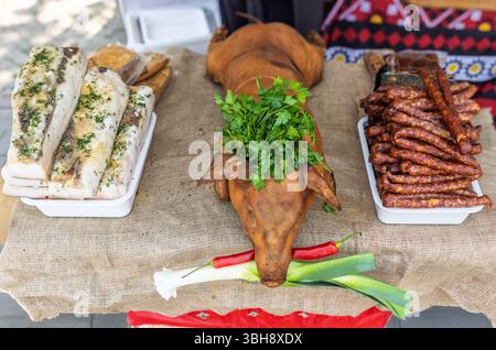 Tradizionale esposizione di carne dell'Europa orientale con un intero suinetto affumicato arrosto, salo (grasso stagionato), salsicce affumicate in un festival di Street food. Un dis festoso Foto Stock