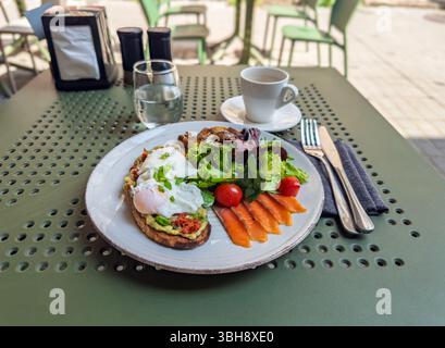 Colazione gourmet su una terrazza all'aperto con uova in camicia su toast all'avocado, salmone affumicato. Colazione sana e estetica con uova in camicia, Foto Stock