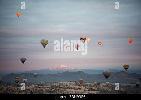 Le mongolfiere si innalzano sulla Cappadocia all'alba, mostrando paesaggi mozzafiato e montagne lontane. Foto Stock