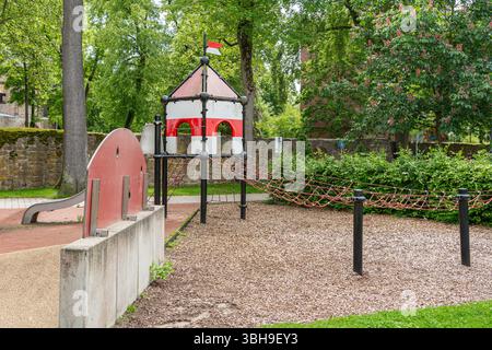 Parco giochi colorato con struttura a tema castello, con scivolo e ponte di corda in un parco lussureggiante. Ideale per attività all'aperto per bambini Foto Stock