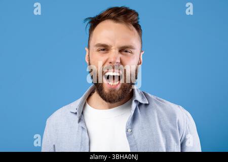 Arrabbiato ragazzo che grida in rabbia, esprimendo la sua aggressione sullo sfondo blu dello studio Foto Stock