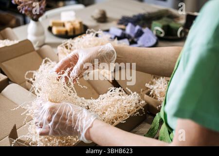 Le mani con i guanti consentono di disporre saponi verdi e lavanda con fiori secchi in confezioni kraft. Prodotti artigianali, imballaggi ecologici, prodotti per la cura della pelle naturali Foto Stock