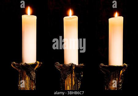 Tre candele bruciate in supporti artistici: Una calda luce a candela con eleganti colonne dorate su sfondo nero, un'atmosfera tranquilla e spirituale Foto Stock
