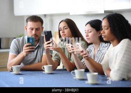 Amici interrazziali che si ignorano a vicenda usando i loro cellulari in cucina a casa Foto Stock