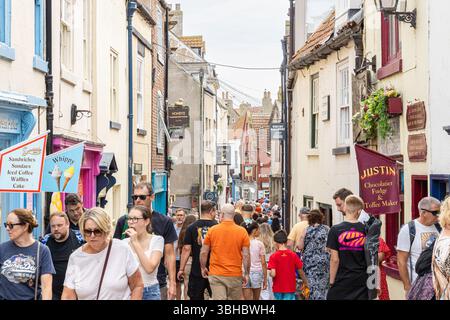 Una vivace scena sulla Whitby's Church Street, mentre la folla di turisti e amanti dello shopping riempie la stretta strada acciottolata costeggiata da negozi storici. Foto Stock