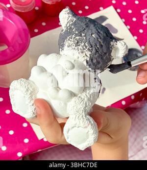 Il bambino impara a dipingere un orsacchiotto in ceramica fatto in casa con il cuore. Il bambino ama gli hobby al coperto e il tempo libero, facendo sculture in ceramica e p Foto Stock