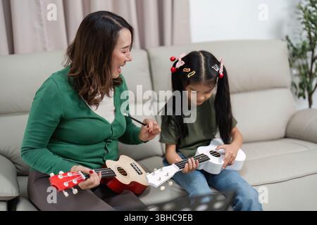 Tempo di musica creativa. Madre e figlia si divertono a giocare con l'ukulele a casa. Foto Stock