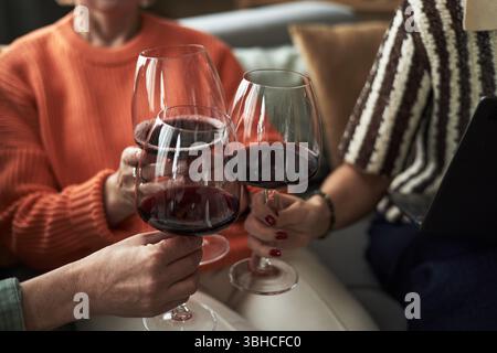 Gruppo di donne caucasiche di mezza età che stringono bicchieri da vino seduti insieme, mani e volti parziali visibili, celebrando l'amicizia durante la riunione delle fidanzate adulte Foto Stock