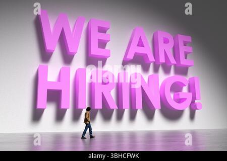 Concetto di ricerca di lavoro con un giovane che cammina vicino a un grande rosa che stiamo assumendo scrivendo su un muro bianco Foto Stock