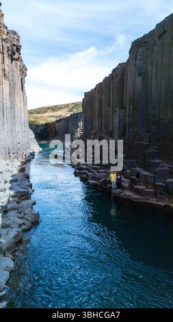 I visitatori si meravigliano davanti alle splendide formazioni del canyon Studlagil in Islanda, dove le acque turchesi scorrono tra le torreggianti colonne di basalto. Una meraviglia naturale mozzafiato ti attende per l'esplorazione. Foto Stock