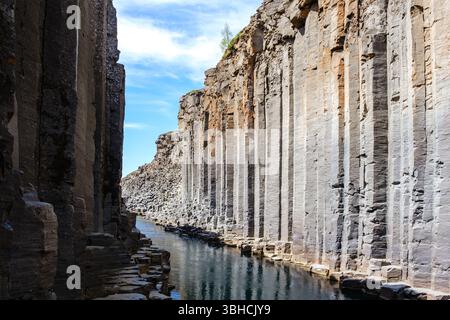 I visitatori si meravigliano davanti alle splendide colonne di basalto e alle tranquille acque del canyon Studlagil in Islanda. Il paesaggio spettacolare offre un'avventura mozzafiato sia per gli amanti della natura che per i fotografi. Foto Stock