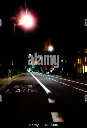 Una corsia degli autobus su una strada buia della città di notte. La strada è illuminata da semafori e la corsia degli autobus è segnata con vernice bianca. Ci sono edifici sull'Eith Foto Stock