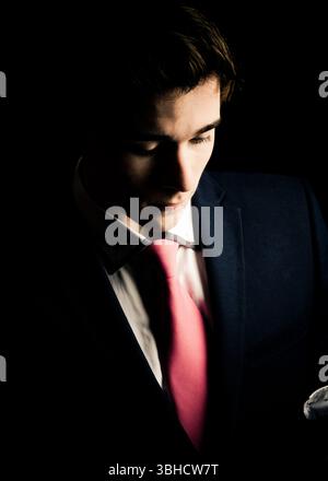 Un giovane uomo, formalmente vestito con vestito e cravatta, guarda verso il basso. L'illuminazione è tenue, creando un'atmosfera suggestiva e contemplativa. L'attenzione è rivolta al Foto Stock