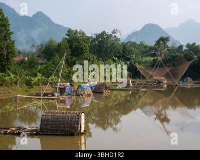 Tranquillo villaggio sul lago tra le montagne vietnamite che mostra tecniche di pesca tradizionali alla luce del mattino presto. Foto Stock