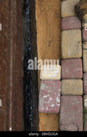 Pietre per pavimentazione posato su base sabbiosa vicino a fondazioni impermeabili nere. Costruzione di piazzali urbani, installazione di viali, ristrutturazione di edifici. Foto Stock