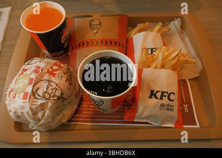 Un classico pasto fast food KFC servito su un vassoio, con due porzioni di patatine fritte, un hamburger di pollo avvolto e due bevande analcoliche. Foto Stock