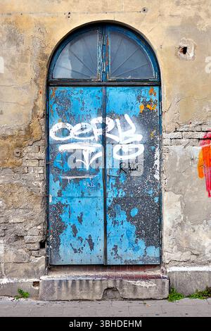 Vecchia porta blu con graffiti sulle pareti intemprate dell'edificio abbandonato Foto Stock