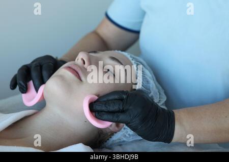 Primo piano del viso di una giovane donna durante la pulizia del viso, estetista con tamponi di cotone. Foto Stock