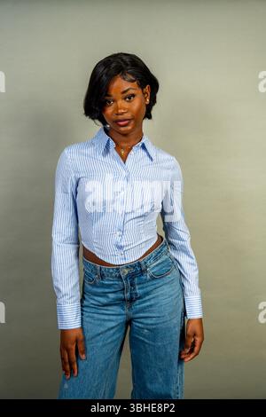 Ritratto in studio di una giovane donna nera con i capelli corti, che indossa una camicia e un jeans a righe blu alla moda, trasudando sicurezza e stile Foto Stock