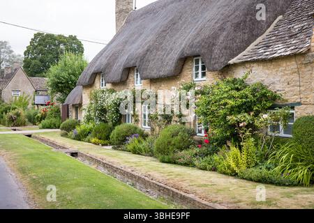 Un tradizionale cottage in paglia con pareti in pietra e lussureggianti giardini a Minster Lovell, un affascinante villaggio dell'Oxfordshire nelle Cotswolds nel Regno Unito Foto Stock