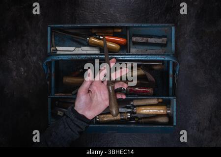 Vecchia lima in metallo con manico in legno tenuto a mano, cassetta degli attrezzi aperta sfocata e superficie in ardesia sullo sfondo dello studio Foto Stock