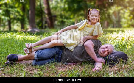 Uomo anziano sdraiato in erba con un bambino seduto su di lui in natura Foto Stock