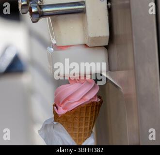 La macchina eroga il gelato rosa morbido servito nel cono per waffle. Il momento cattura la deliziosa delizia preparata in una posizione soleggiata Foto Stock