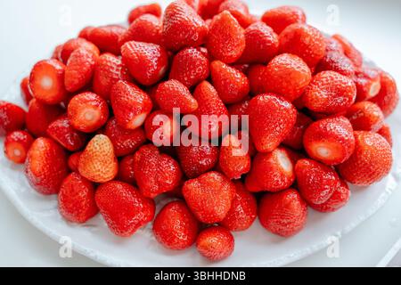 Un grande mucchio di fragole mature esposte su un piatto bianco. I vivaci e succosi frutti rossi creano un'allettante visuale, sottolineandone la naturale natura Foto Stock