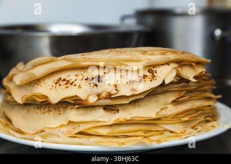 I pancake pronti sono sul tavolo, in un piatto bianco, accanto a una ciotola in acciaio inox sul tavolo. Foto Stock