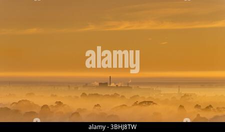 Fumo nebbia a bassa nuvola Vista distante della fabbrica industriale all'alba del mattino presto luce arancione Geelong, Victoria, Australia. Foto Stock