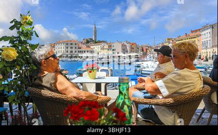 I turisti seduti in un caffè sul fronte del porto ammirano la vista della città vecchia al porto, Rovigno, Istria, Croazia, Europa Foto Stock