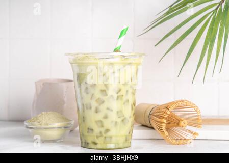 Bevanda fredda verde con latte matcha. Delizioso tè verde matcha freddo mescolato con cubetti di ghiaccio e latte cremoso montato nel bicchiere del latte su sfondo bianco del tavolo Foto Stock